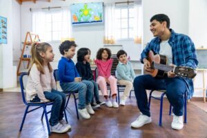 Diverse group of 7 year olds at school having fun in music class with male cheerful teacher.