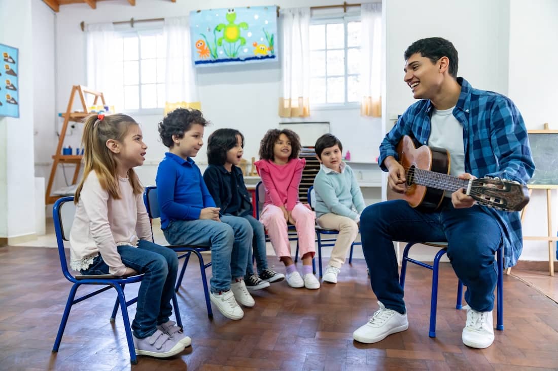Diverse group of 7 year olds at school having fun in music class with male cheerful teacher.