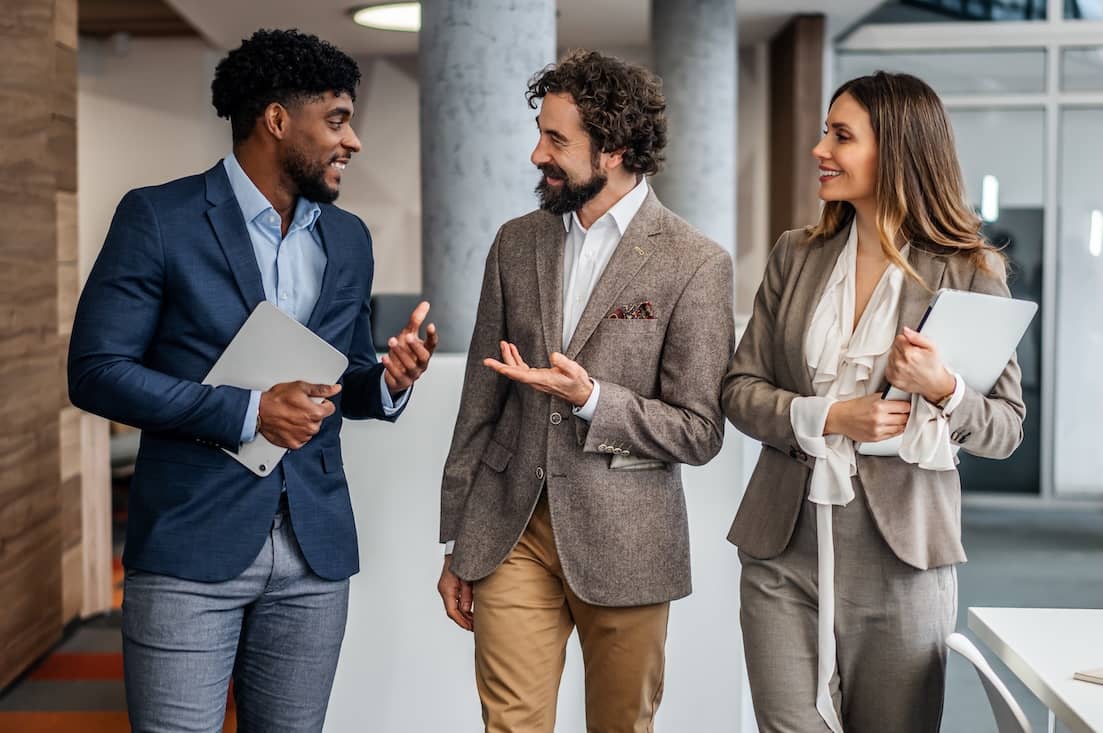Three business professionals walking through a modern office building hallway.
