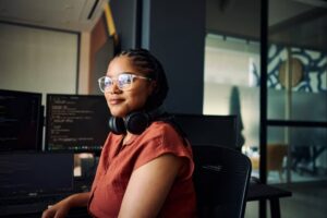 Young woman programmer coding on dual monitors in a modern office environment.