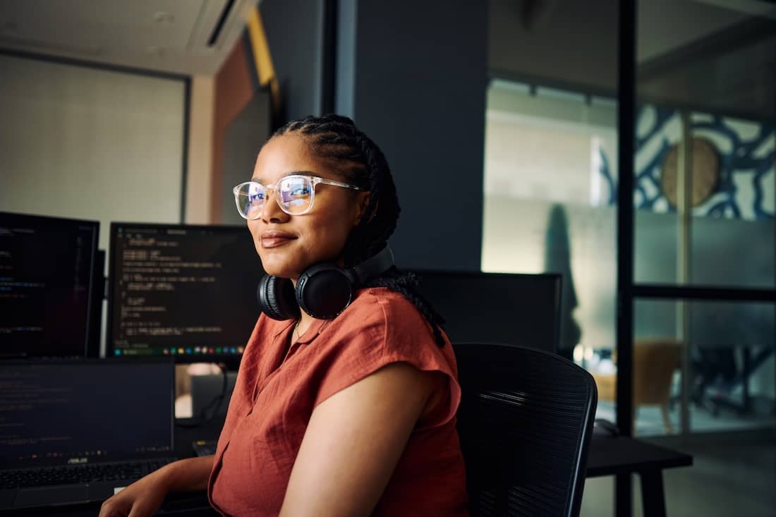 Young woman programmer coding on dual monitors in a modern office environment.