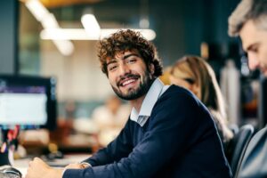 Young adult man smiling at office workspace.