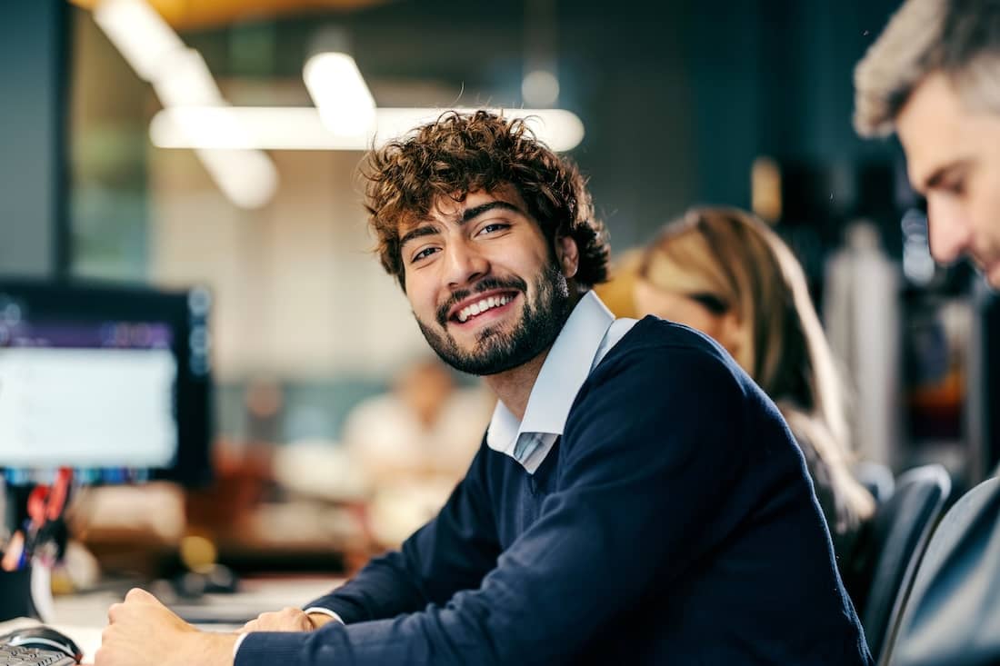 Young adult man smiling at office workspace.
